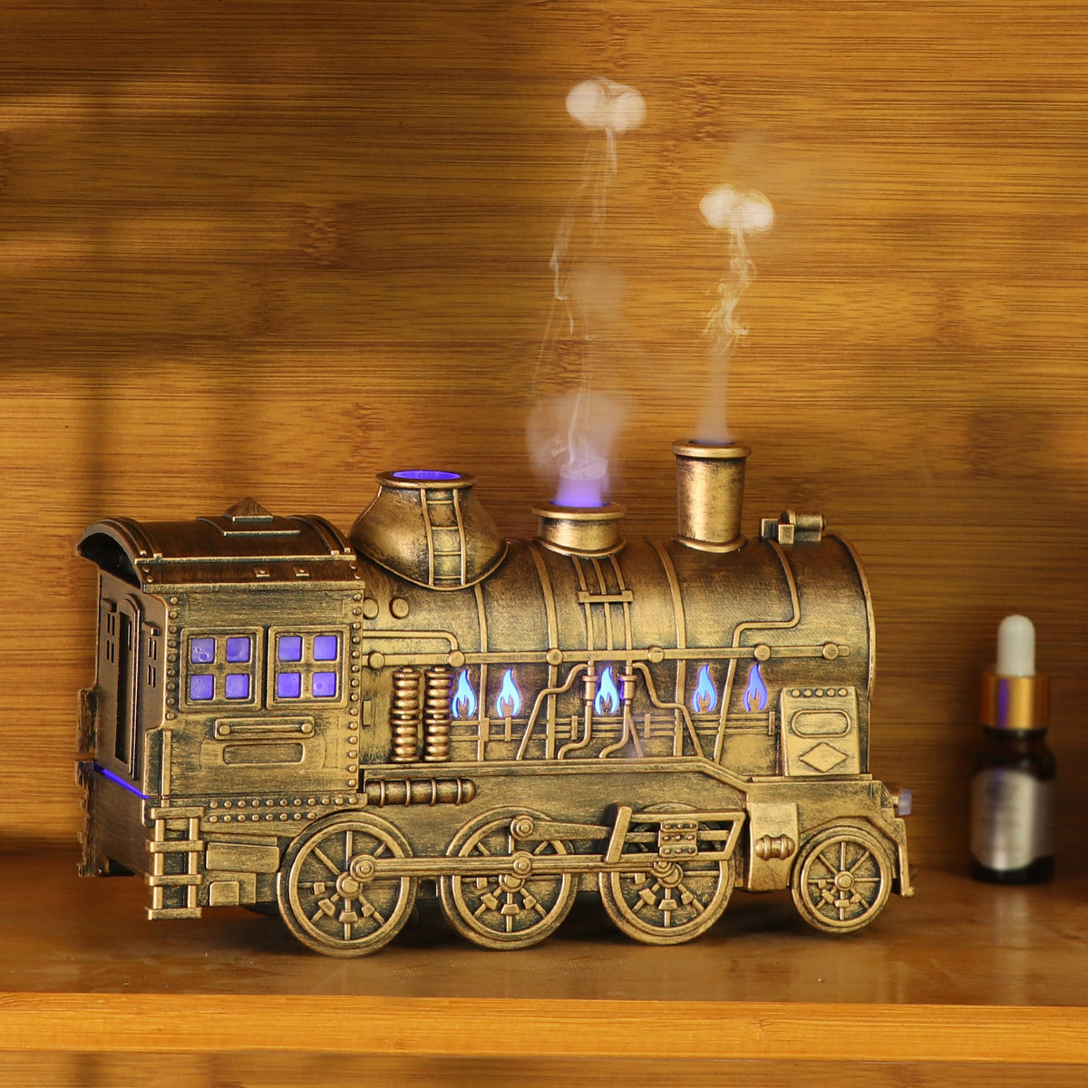 Antique gold steam train essential oil diffuser with glowing cabin lights and rising mist beside an essential oil bottle